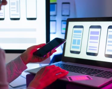 Kobieta przy laptopie trzymająca telefon w dłoni